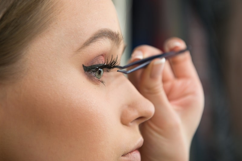 beautiful woman applying fake eyelashes with tweezers