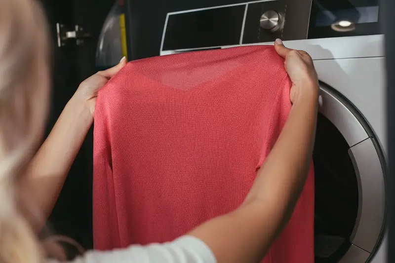 cropped view of housewife holding pullover near washing machine