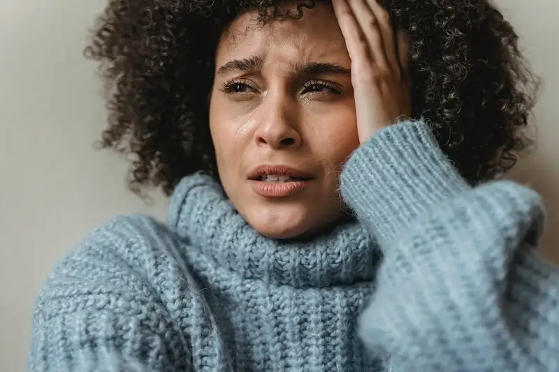 attractive black woman wearing false eyelashes crying in despair holding her head with left hand