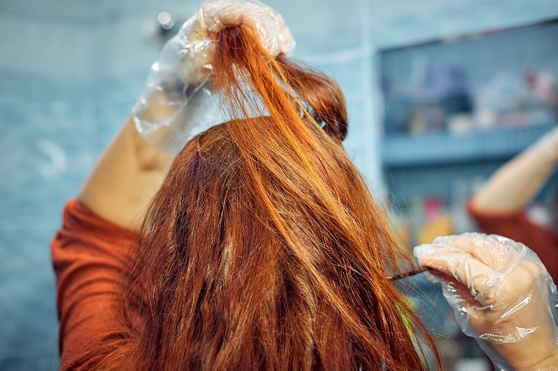 close-up of a red haired woman dyeing her hair at home