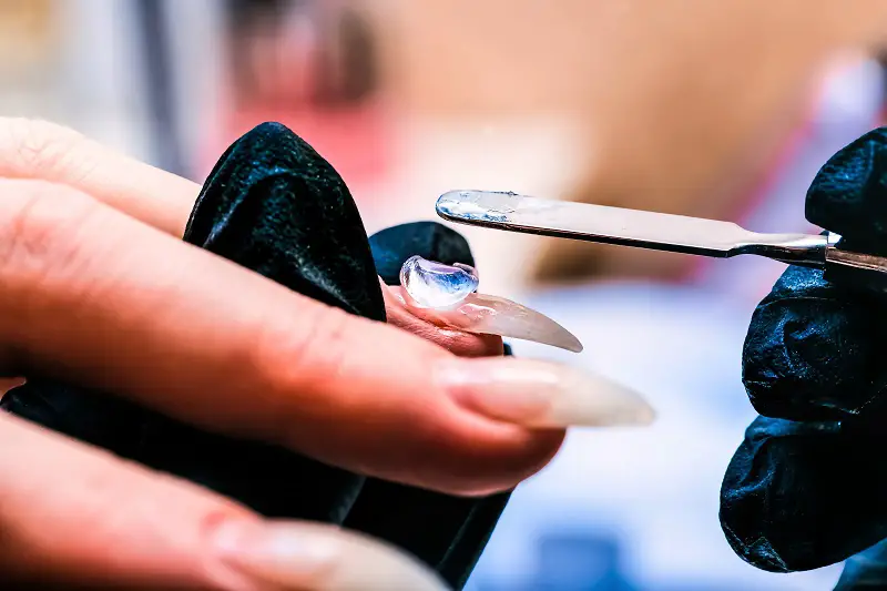 close-up of a manicurist applying a base layer of polygel to natural nails with a metal spatula
