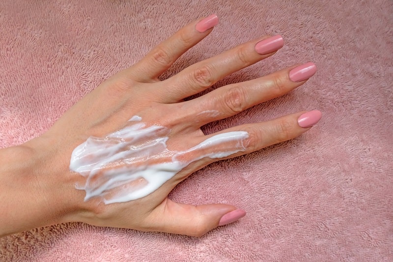 close-up of a woman's hand with pink nail polish and sun tan lotion on the back of the hand