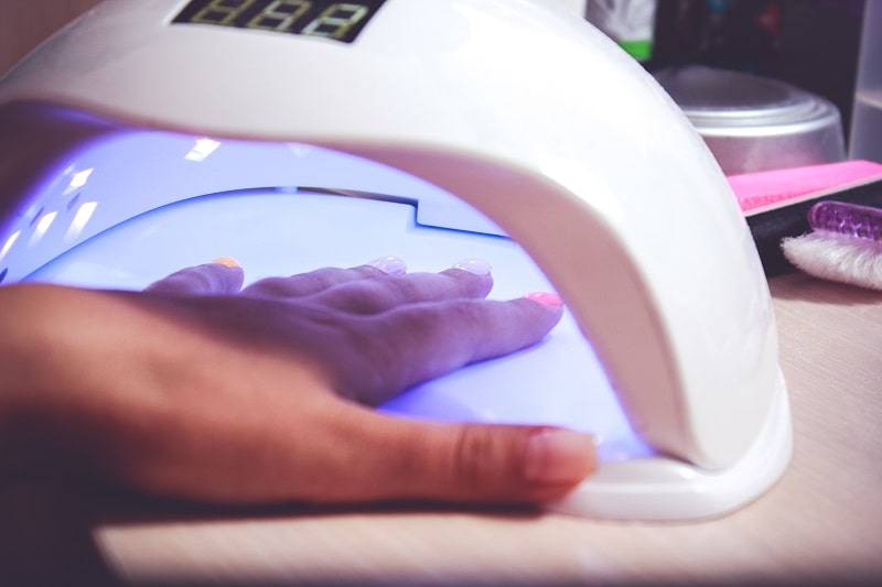close-up of a woman curing her polygel nails in an LED nail lamp
