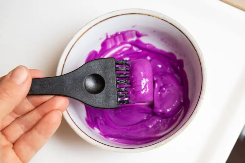 ceramic bowl containing mixed pastel purple hair dye and a hair dye brush
